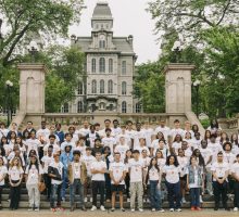 Group of students in SummerStart t-shirts standing together, with Hall of Languages building in background.