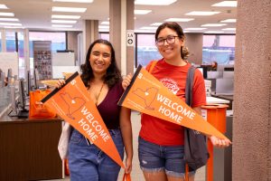 Two smiling students holding orange pendants with writing "Welcome Home"