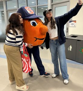 Two students taking a selfie with Otto, the orange, SU's mascot.