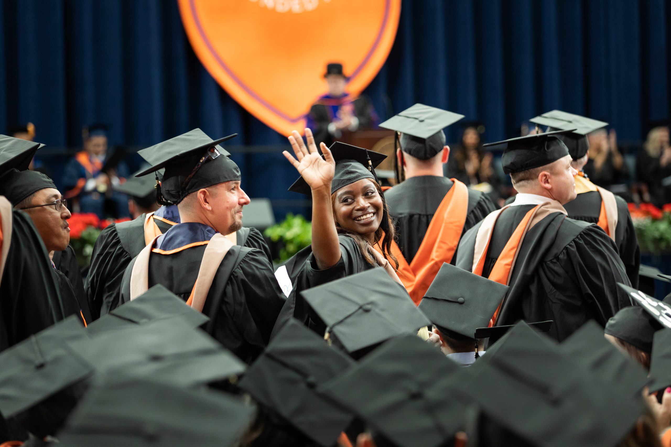 Student in graduation attire at convocation waving.